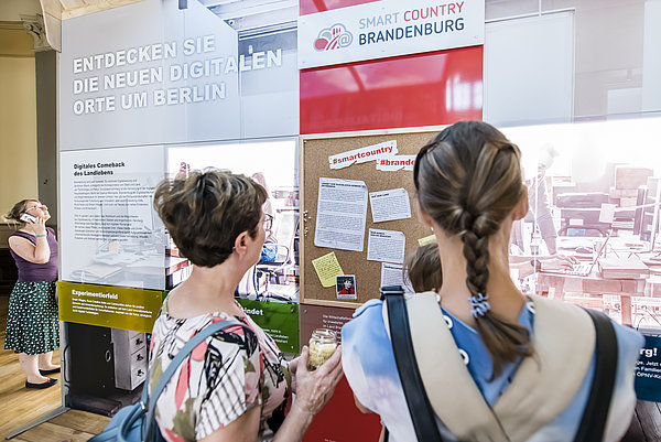 Foto: Zwei Personen schauen sich eine Infowand zum Thema Smart Country Brandenburg an. © WFBB | David Marschalsky