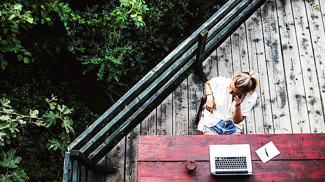 Blick von oben auf Frau mit Laptop, die auf der Terrasse sitzt