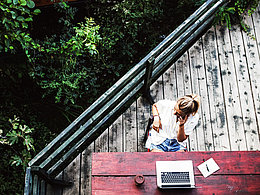 Blick von oben auf Frau mit Laptop, die auf der Terrasse sitzt