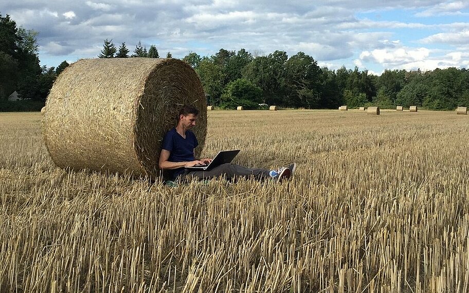 Person sitzt mit seinem Laptop an einem Strohballen