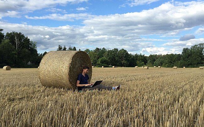 Person sitzt mit seinem Laptop an einem Strohballen