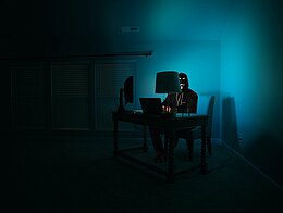 Ein Mann an einem Computer, der als anonymer Hacker verkleidet ist und eine Guy-Fawkes-Maske trägt.