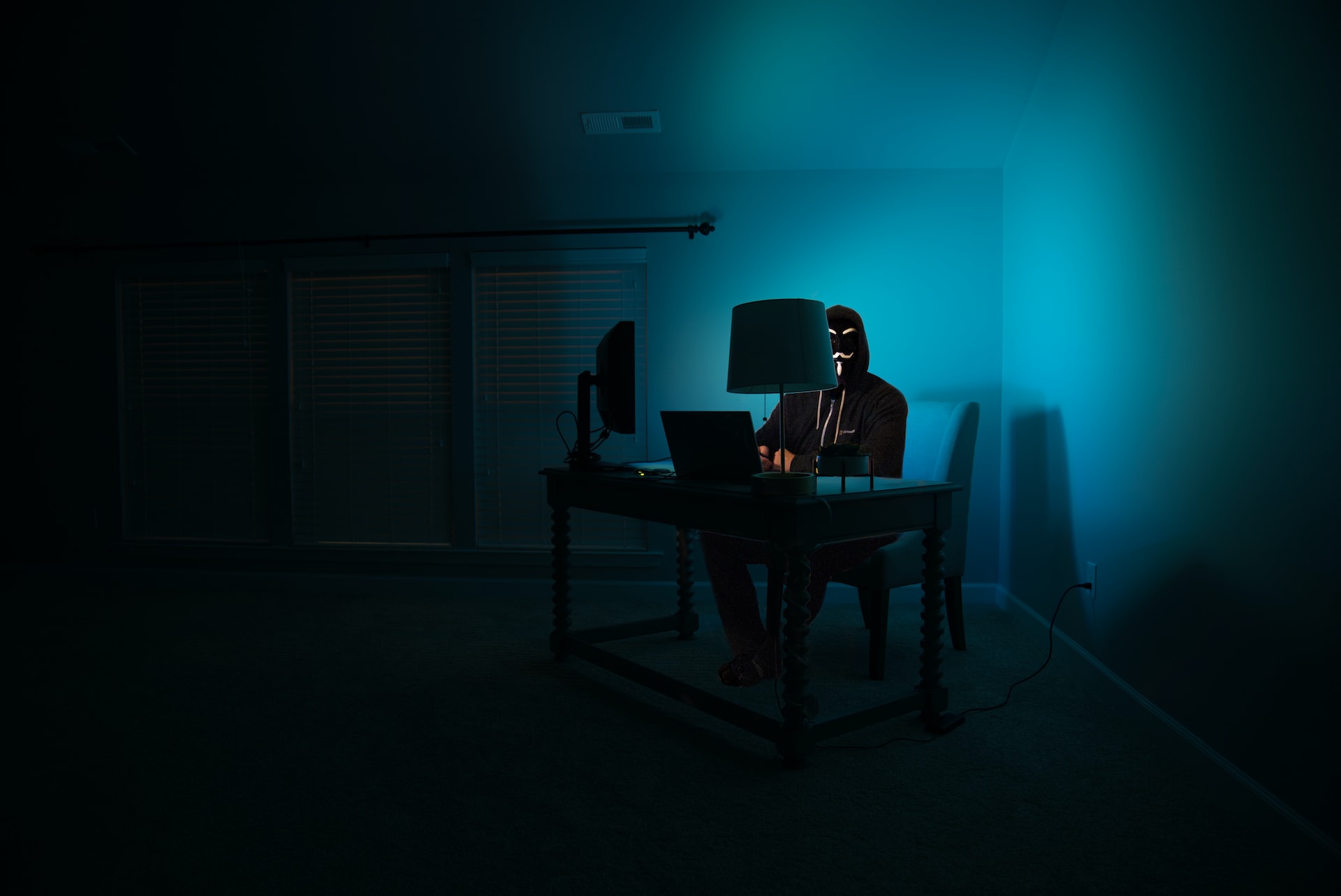 Ein Mann an einem Computer, der als anonymer Hacker verkleidet ist und eine Guy-Fawkes-Maske trägt.
